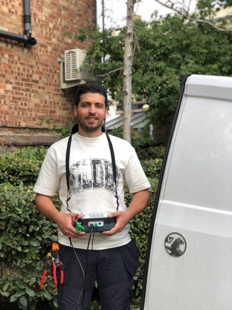 Electrician Chiswick holding electrical testing equipment beside company van