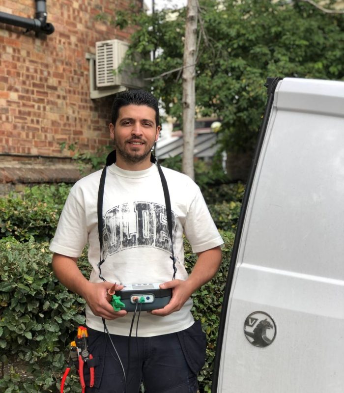 Electrician Chiswick holding electrical testing equipment beside company van
